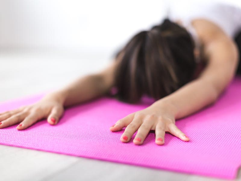 Woman in child's pose on a pink pilates mat